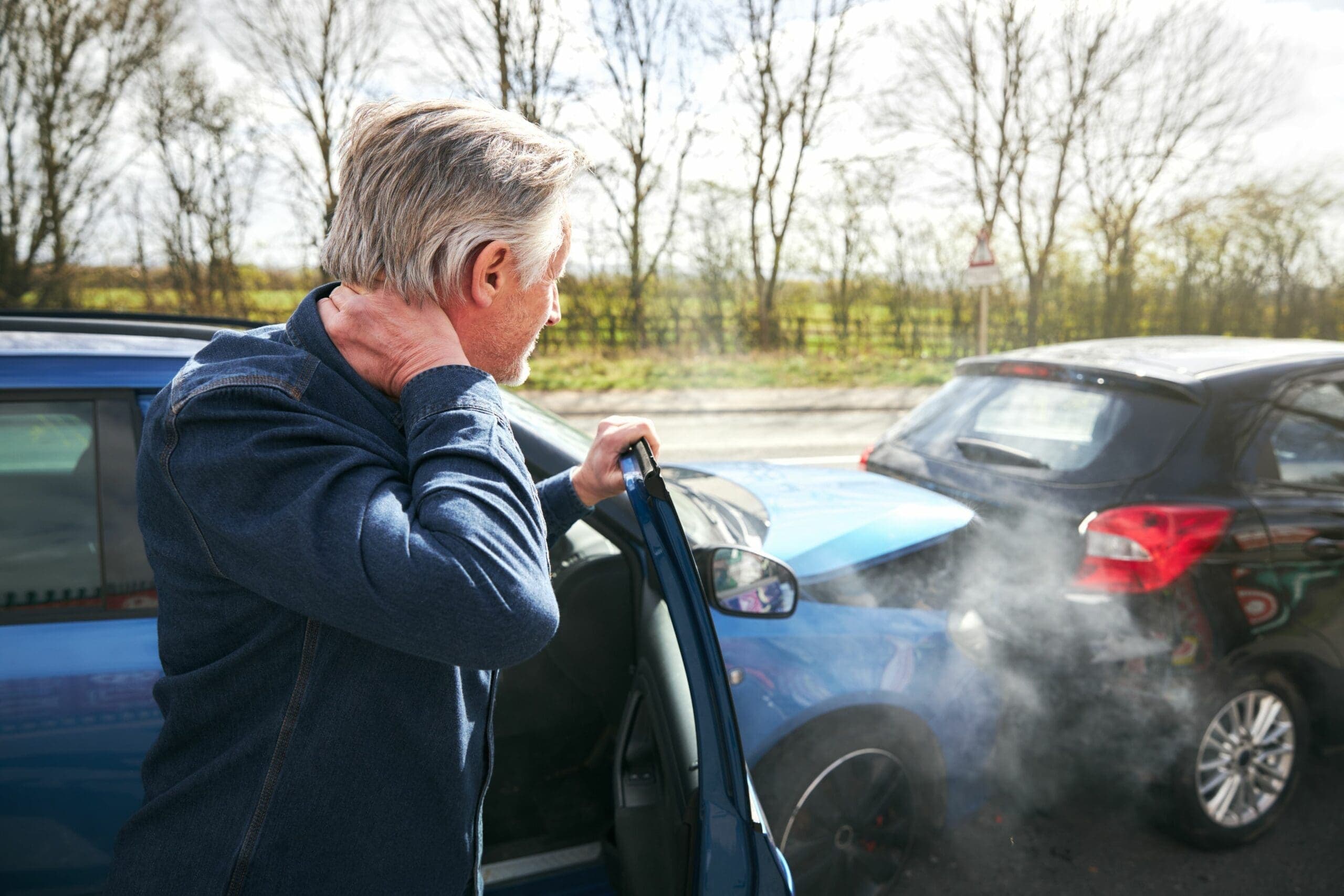 Driver holding his neck beside his rear-ended car after a crash, representing an uninsured driver's injury claim in Nevada.