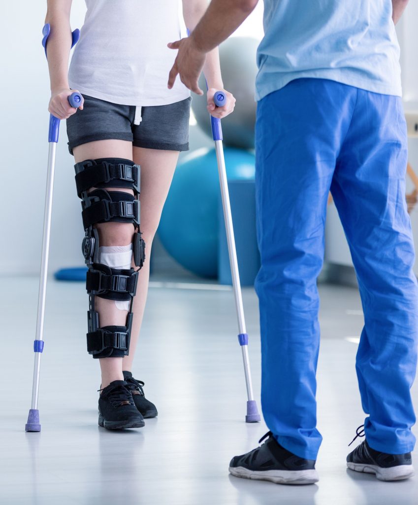 Woman with knee brace and crutches stands next to a man with leg brace, possibly requiring a product defect attorney.