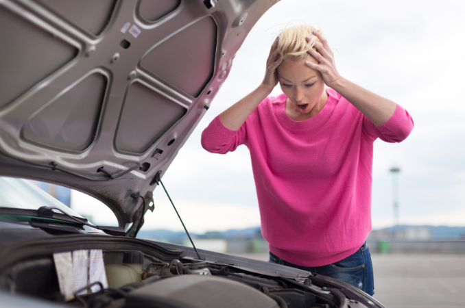 A woman, troubled by her car, holds her head while inspecting the engine. Seeking assistance from a product defect attorney.